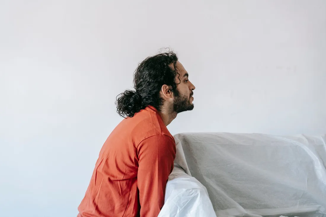 Mann stützt sich auf ein in Schutzfolie eingepacktes Sofa vor heller Wand