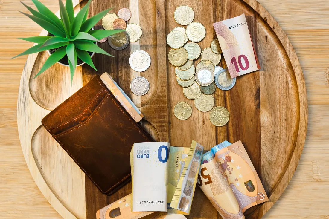 Euroscheine, Münzen und eine Geldbörse liegen auf einem runden Holzbrett