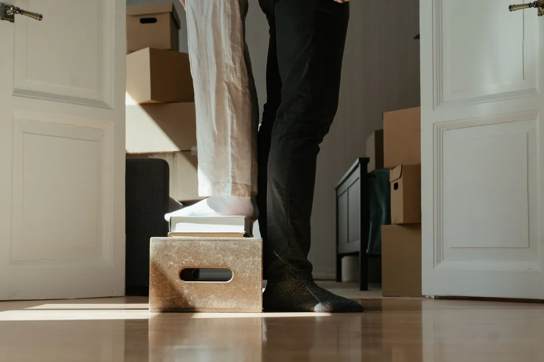 Person steht auf einer kleinen Kiste zwischen gepackten Kartons im Zimmer