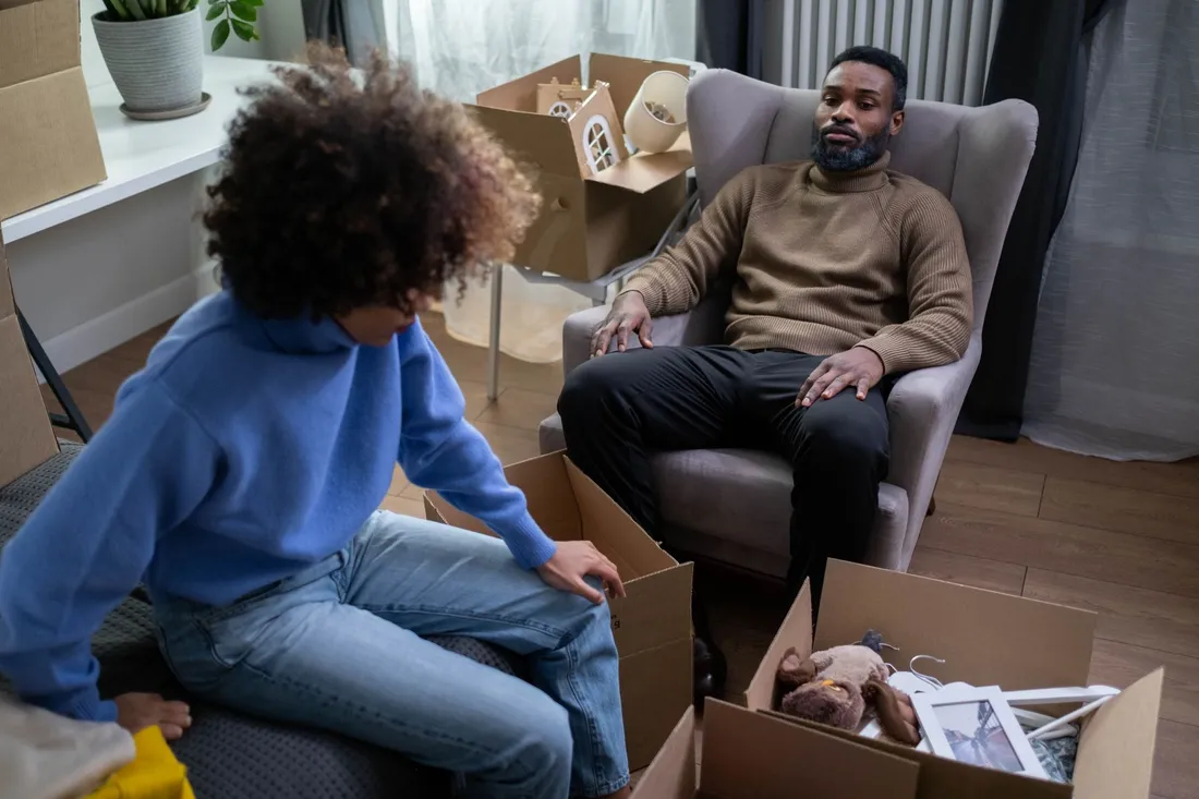 Zwei Personen packen im Wohnzimmer zwischen offenen Kartons Sachen aus